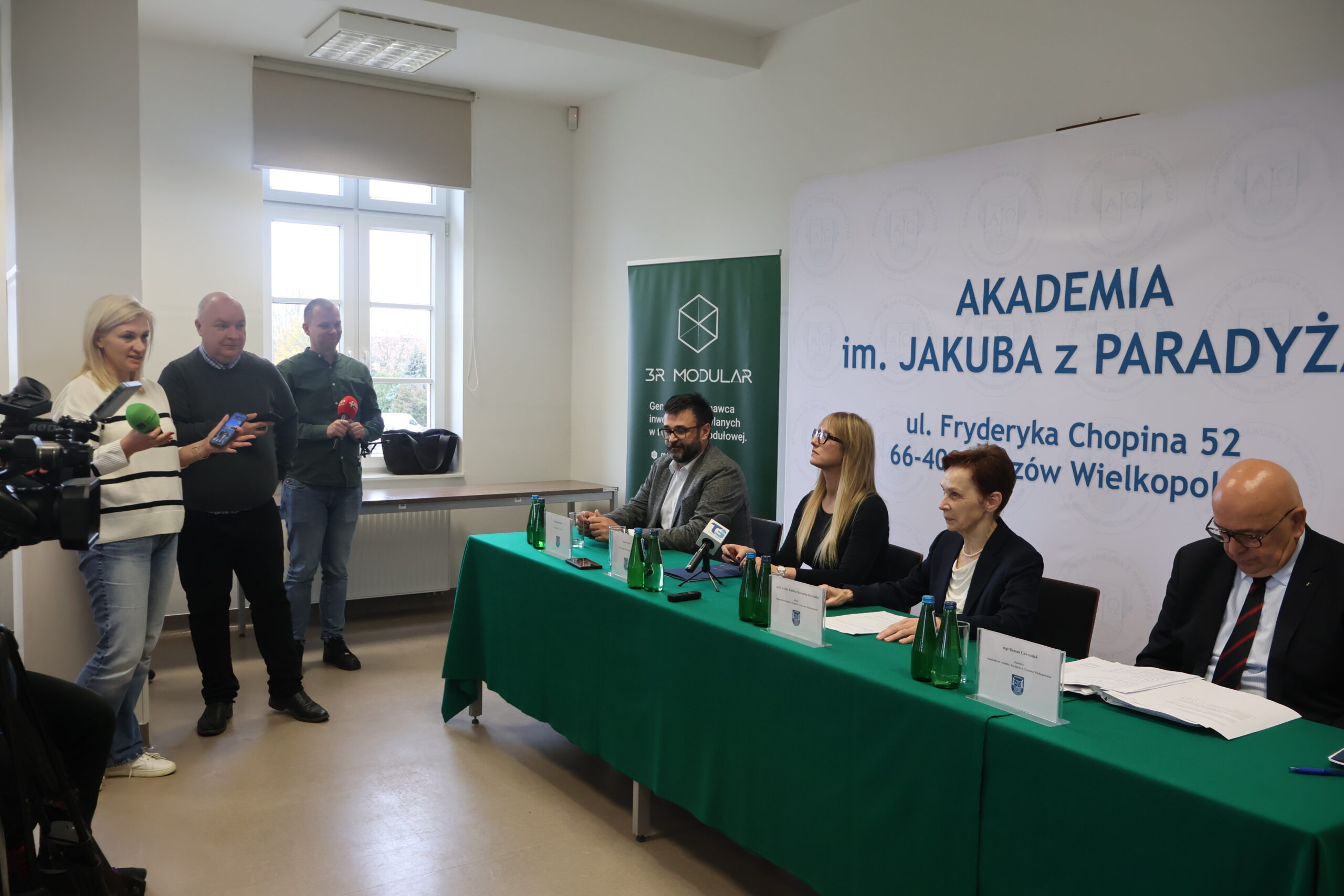 Na zdjęciu od prawej za stołem: mgr Roman Gawroniak, Rektor Akademii im. Jakuba z Paradyża - prof. dr hab. Elżbieta Skorupska-Raczyńska, Prezes Zarządu Wykonawcy 3R MODULAR Pani Joanna Sypko,Przedstawiciel firmy CLIMATIC Pan Aleksander Panek podczas podpisania umowy o budowę nowego budynku 3bis na terenie przy ul. Fryderyka Chopina 52. Po lewej stoją lokalne media.