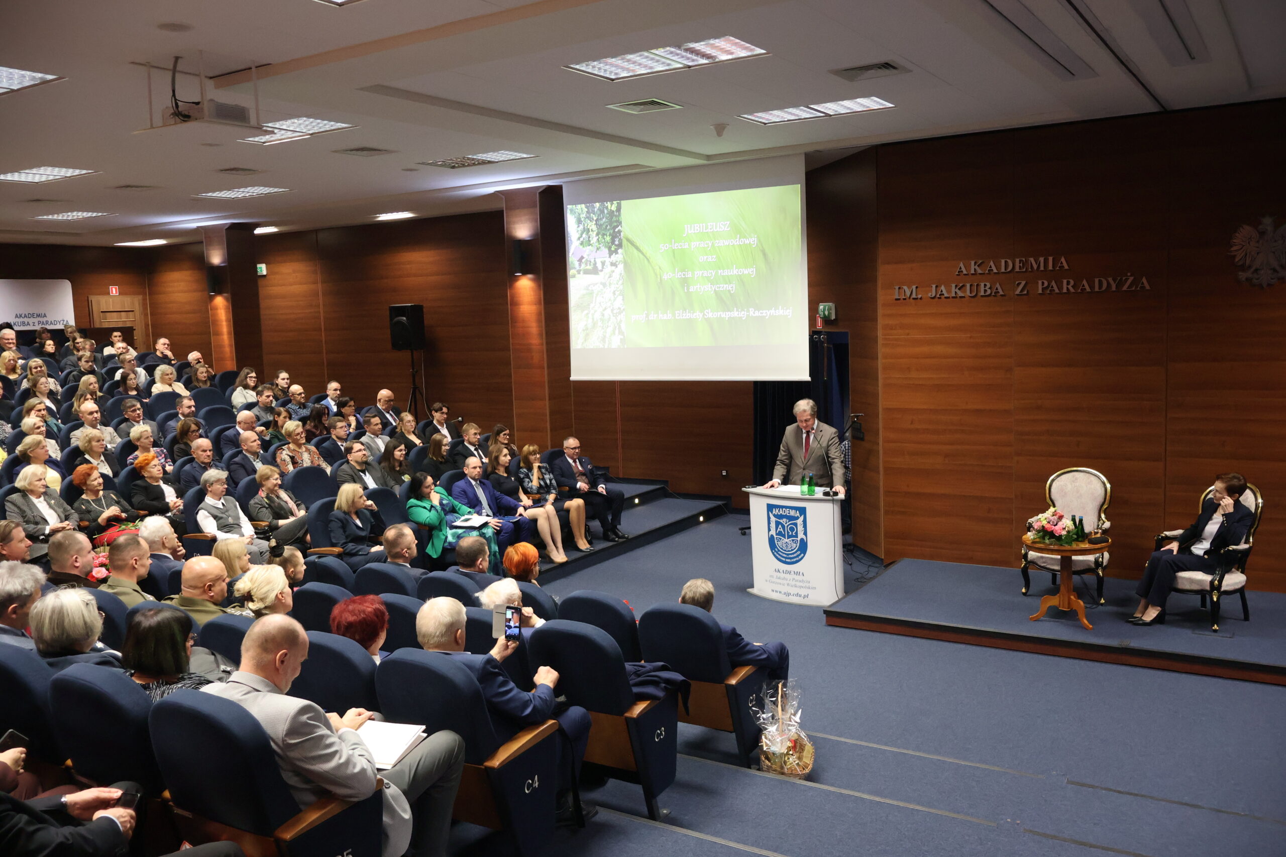 Na zdjęciu przemawia Prorektor ds. Nauki prof. dr hab. Grzegorz Kucharczyk oraz na fotelu siedzi Rektor Uczelni prof. dr hab. Elżbieta Skorupska-Raczyńska.