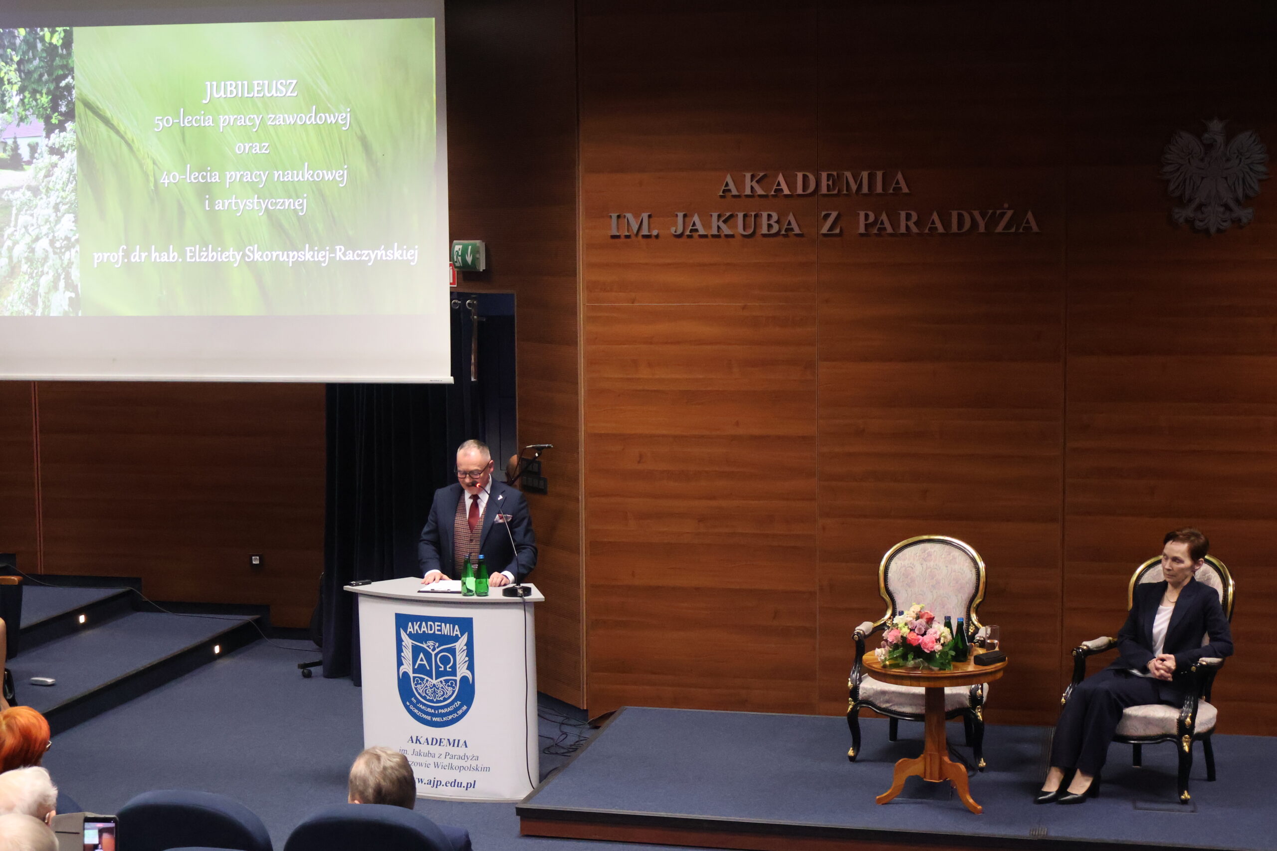 Na zdjęciu przemawia dr Wojciech Kuska oraz na fotelu siedzi Rektor Uczelni prof. dr hab. Elżbieta Skorupska-Raczyńska.