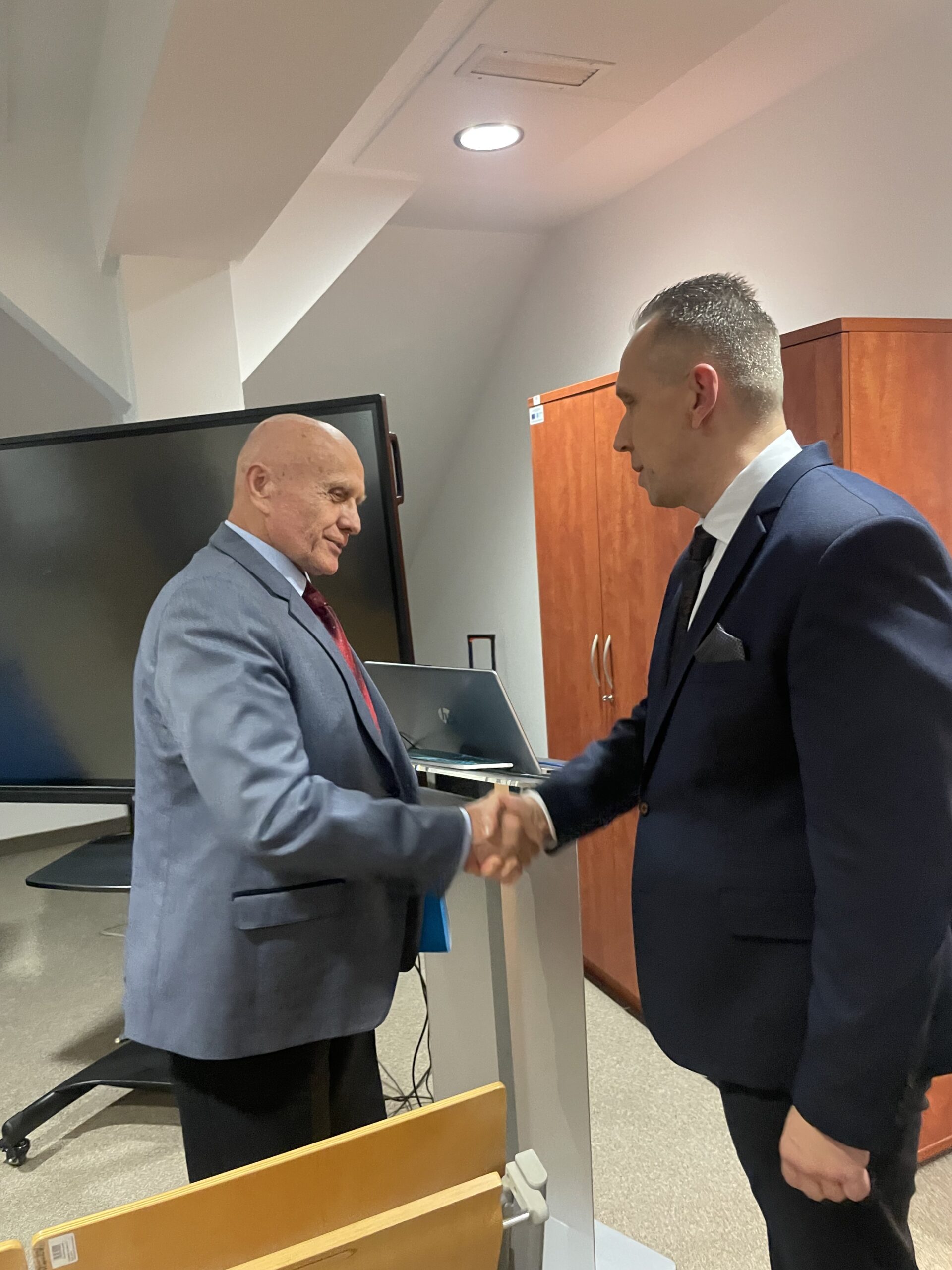 Promotor gratuluje swojemu doktorantowi podając mu dłoń.