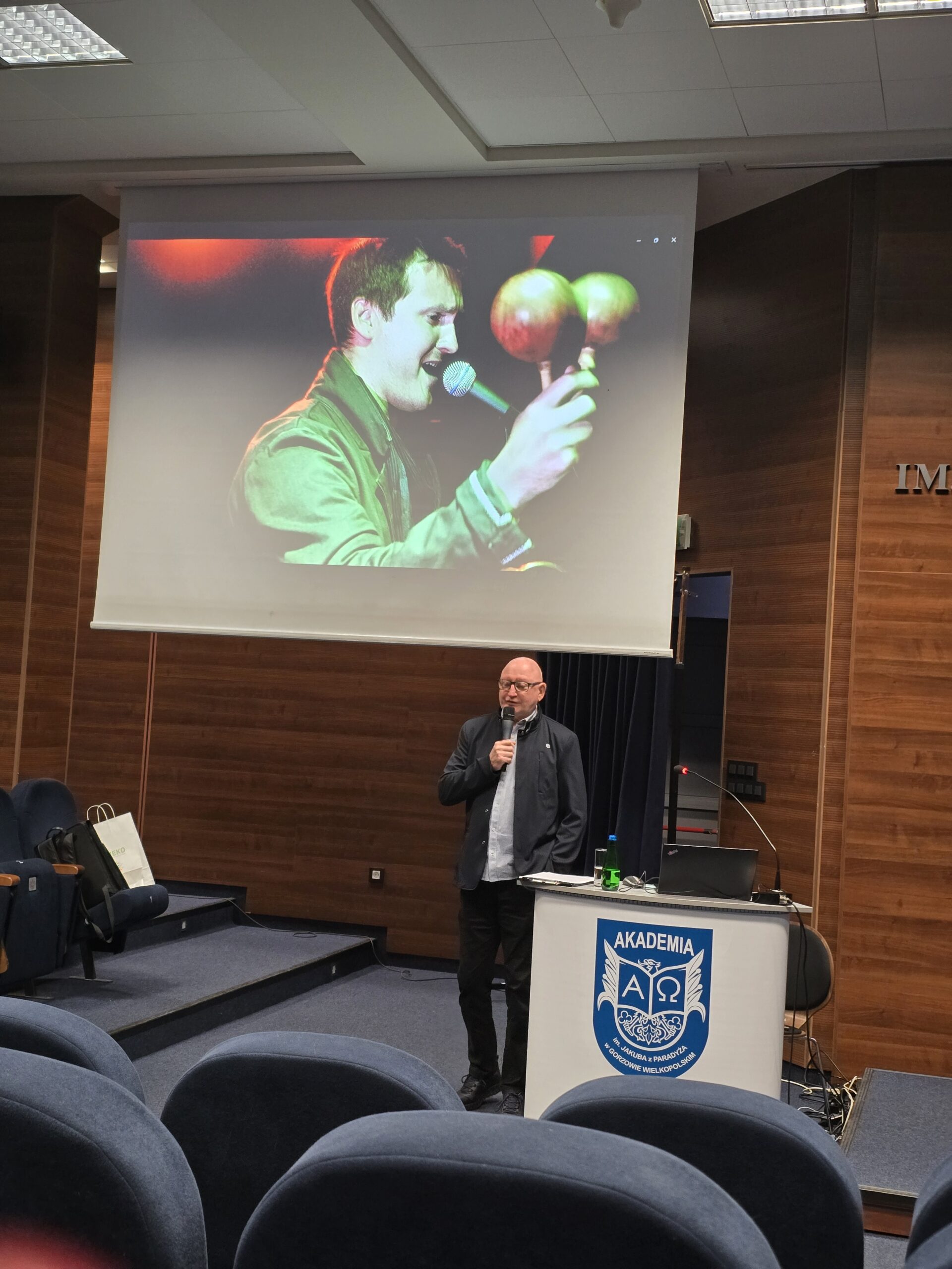 Mężczyzna z mikrofonem stoi obok mównicy podczas konferencji.