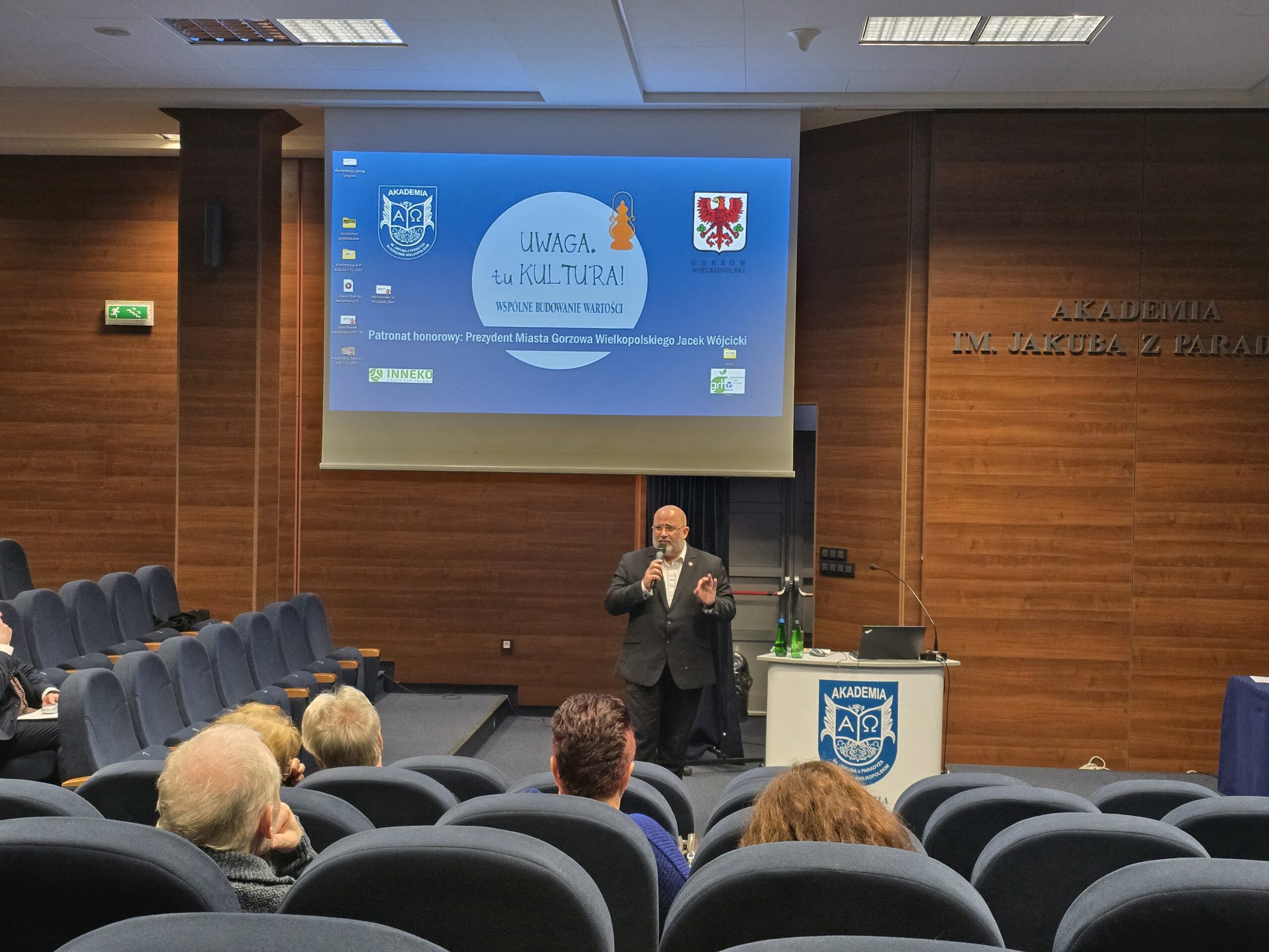 Mężczyzna z mikrofonem stoi obok mównicy podczas konferencji.