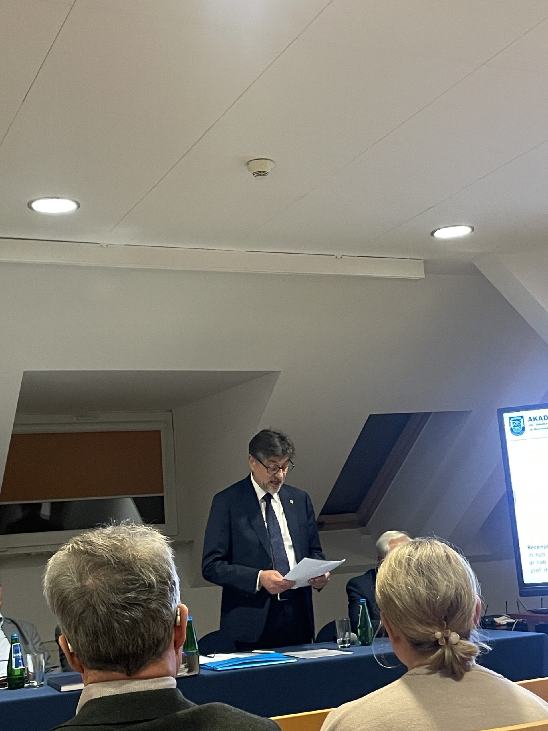 Trzeci członek z komisji z kartkami w rękach przemawia do zgromadzonych.