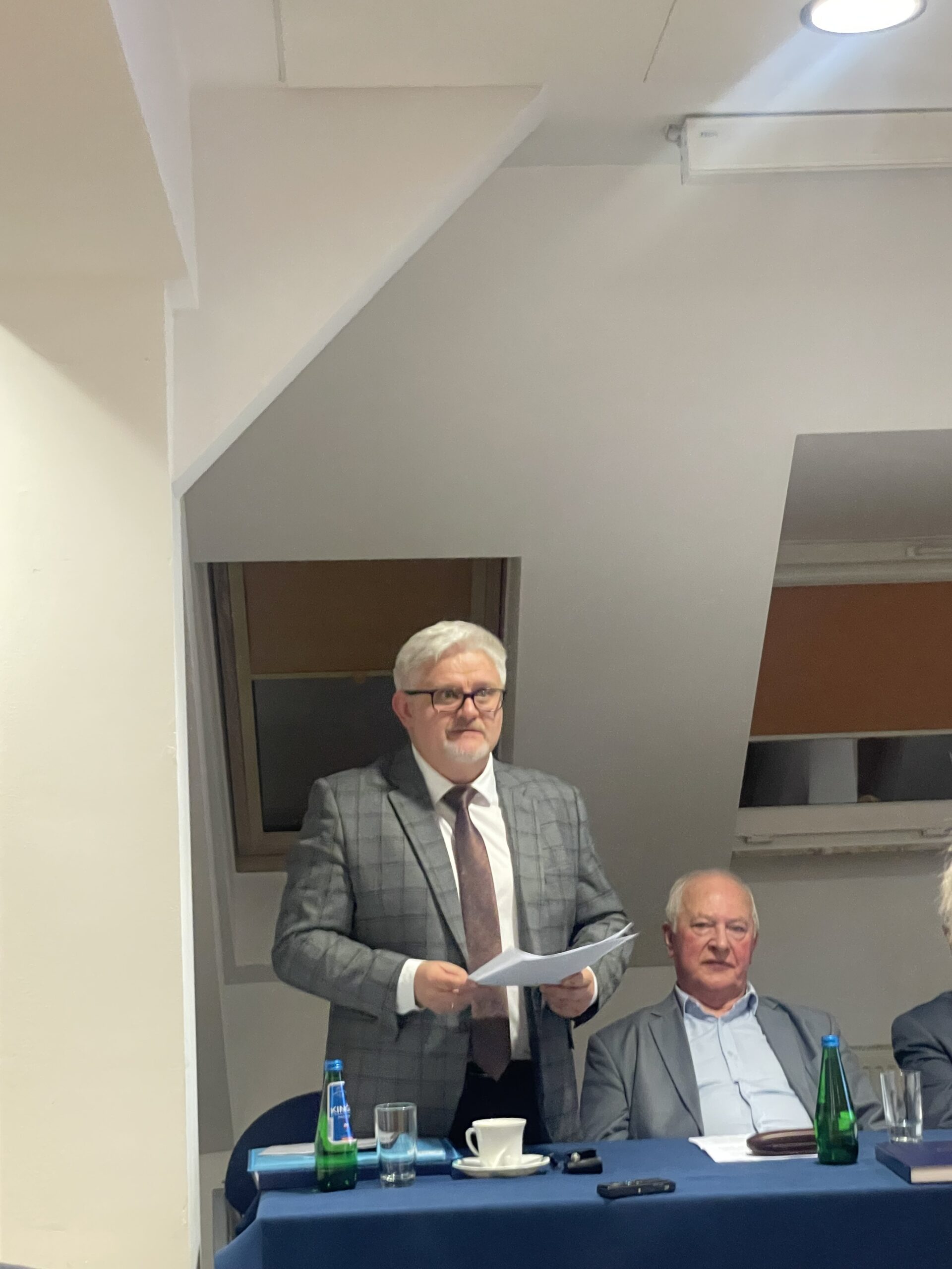 Kolejny członek komisji z kartkami w rękach przemawia do zgromadzonych.