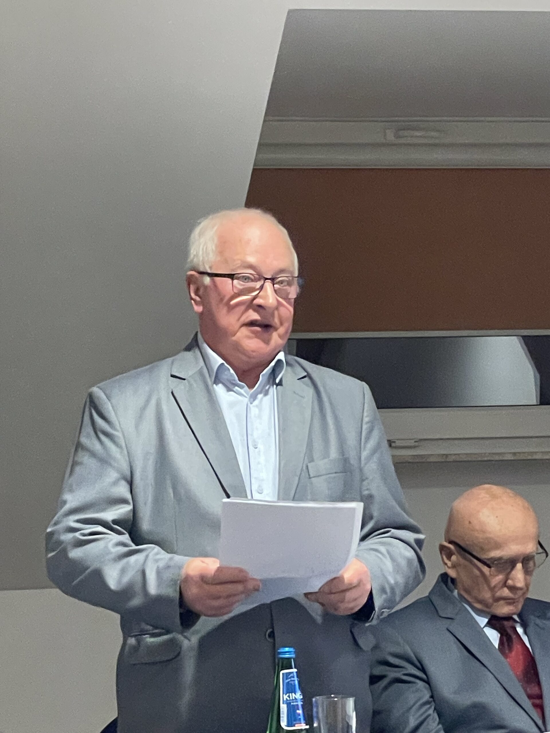 Członek komisji z kartkami w rękach przemawia do zgromadzonych.