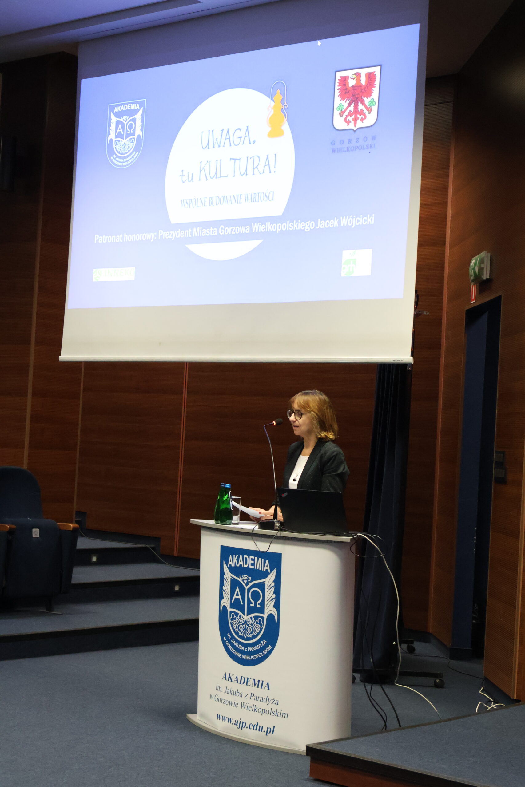 Wykładowca Uczelni stoi za mównicą podczas konferencji.