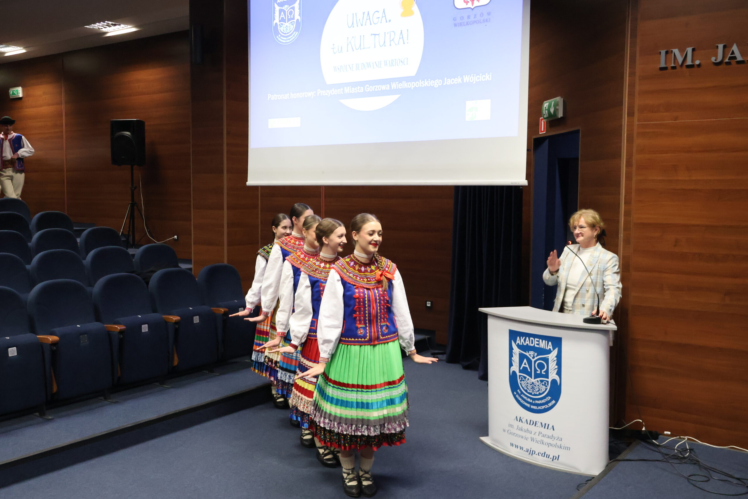 Kobiety z Zespołu Mali Gorzowiacy wchodzą na występ. Po prawej kobietą za mównicą.