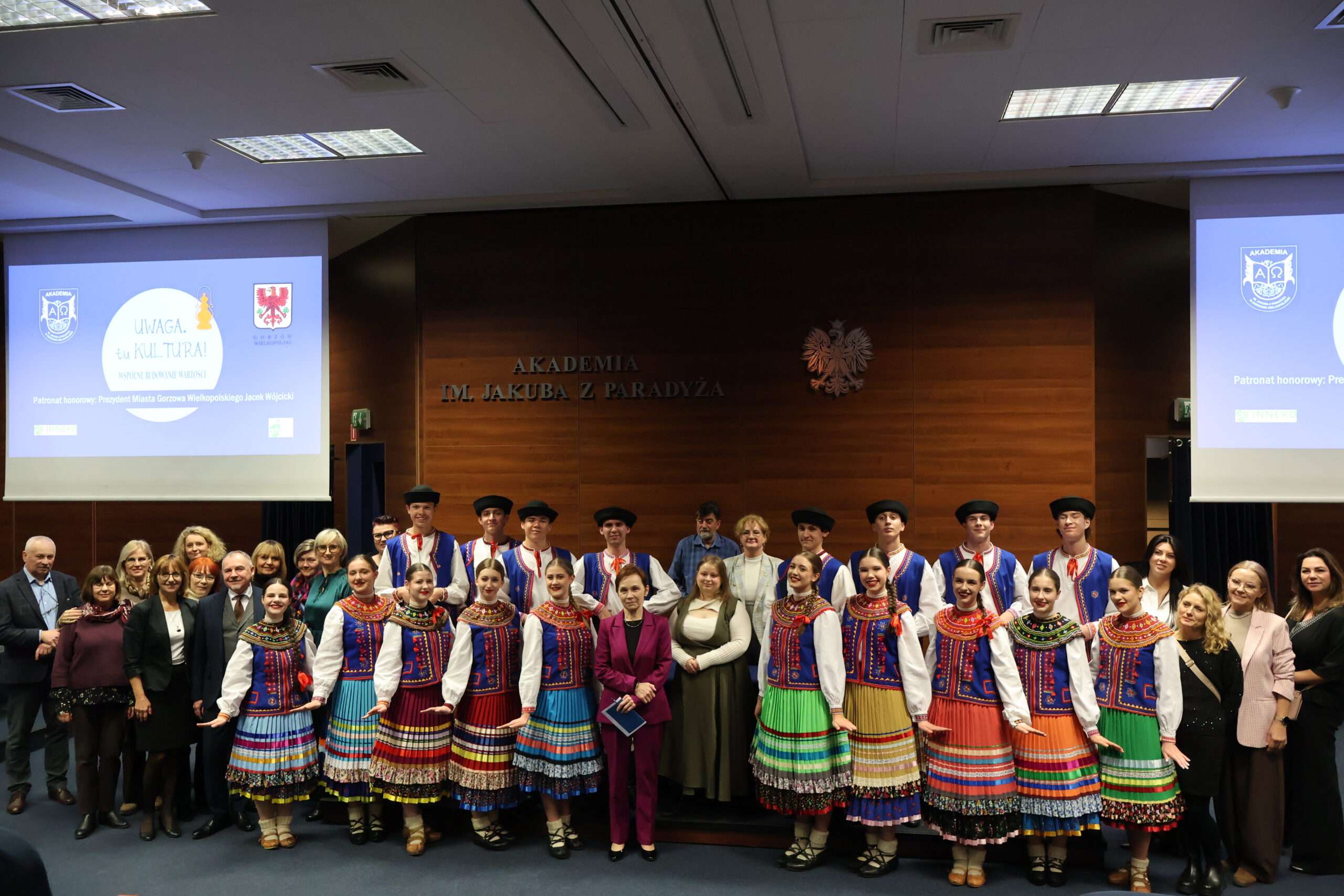 Grupa osób pozuje do grupowego zdjęcia. Na środku stoi Pani Rektor wraz z uczestnikami Zespołu Tanecznego Mali Gorzowiacy i uczestnikami konferencji.