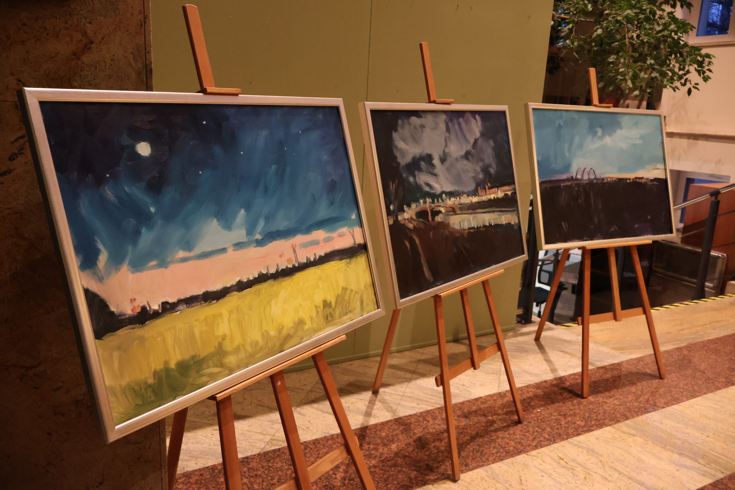 Trzy obrazy stojące na sztalugach przedstawiające pejzaże miasta Gorzowa Wielkopolskiego.