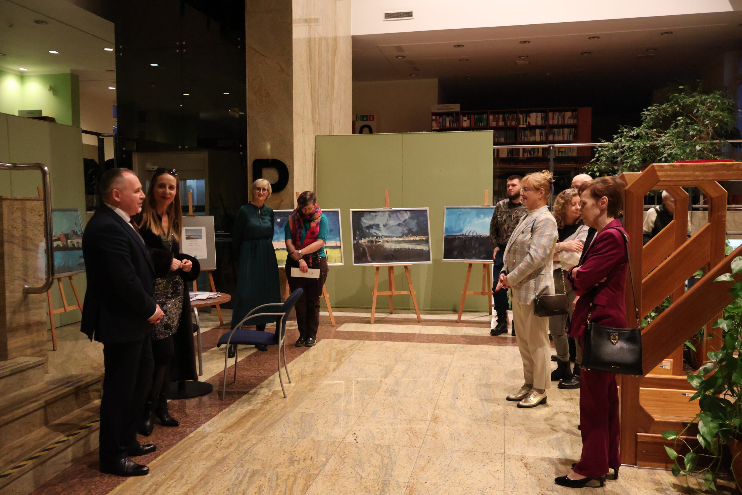 Grupa osób podczas wystawy malarstwa. Po prawej stronie stoi Pani Rektor, po lewej malarka i wykładowca.