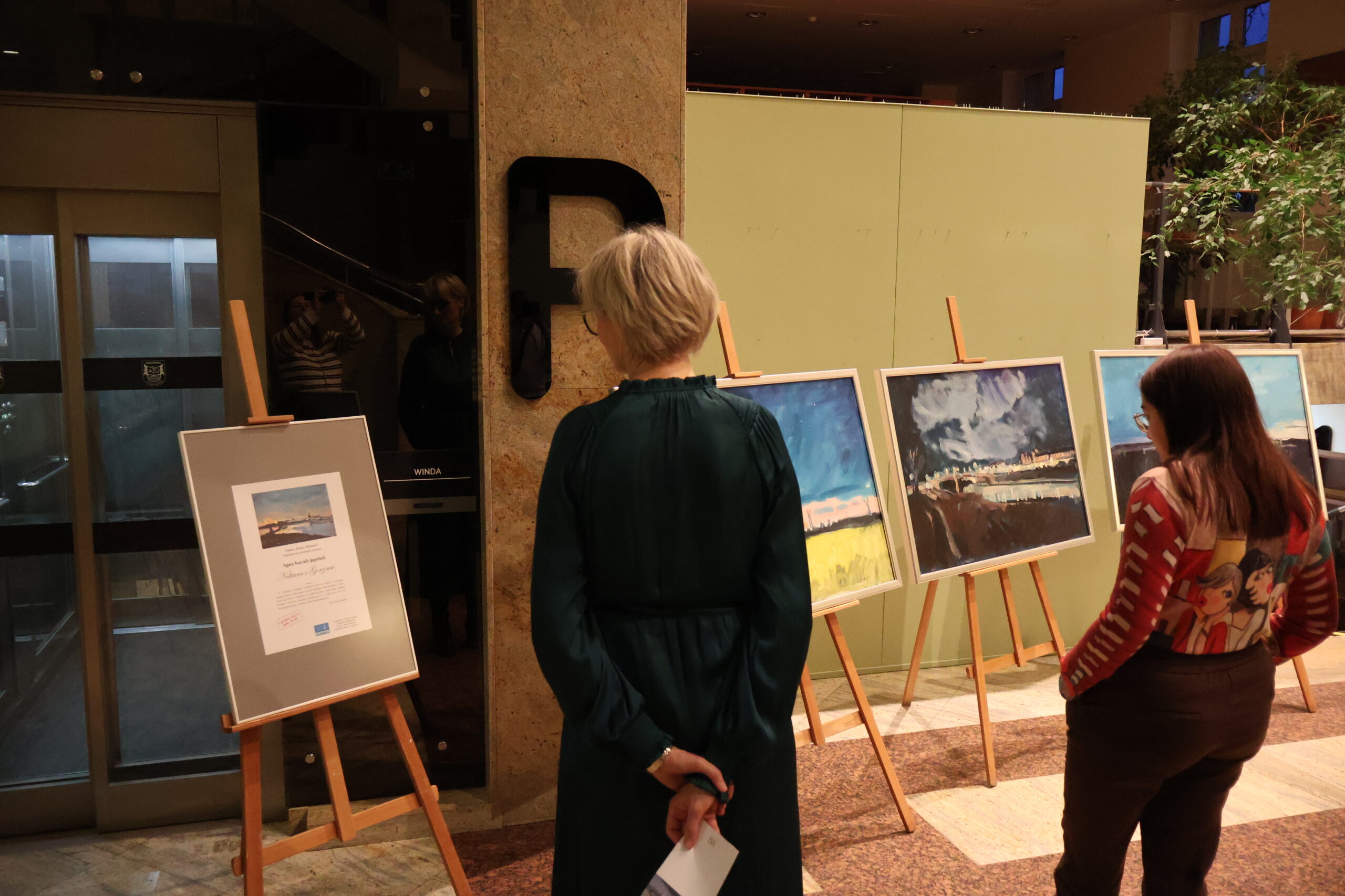 Dwie kobiety oglądające obrazy na wernisażu.
