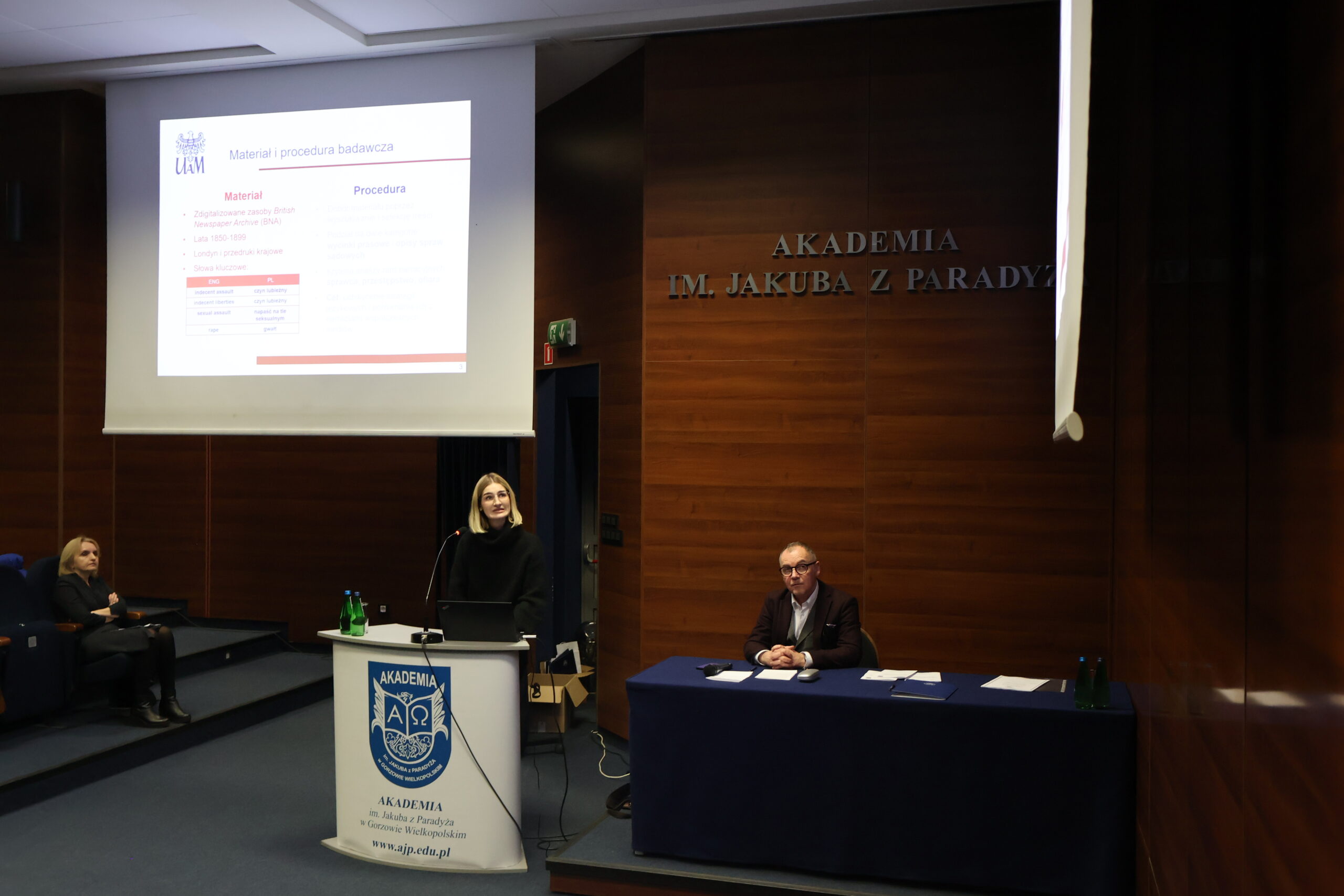 Prelegentka wygłaszająca swój referat podczas konferencji, za stołem prezydialnym dr Wojciech Kuska, a w tle prof. AJP dr hab. Agnieszka Niekrewicz.