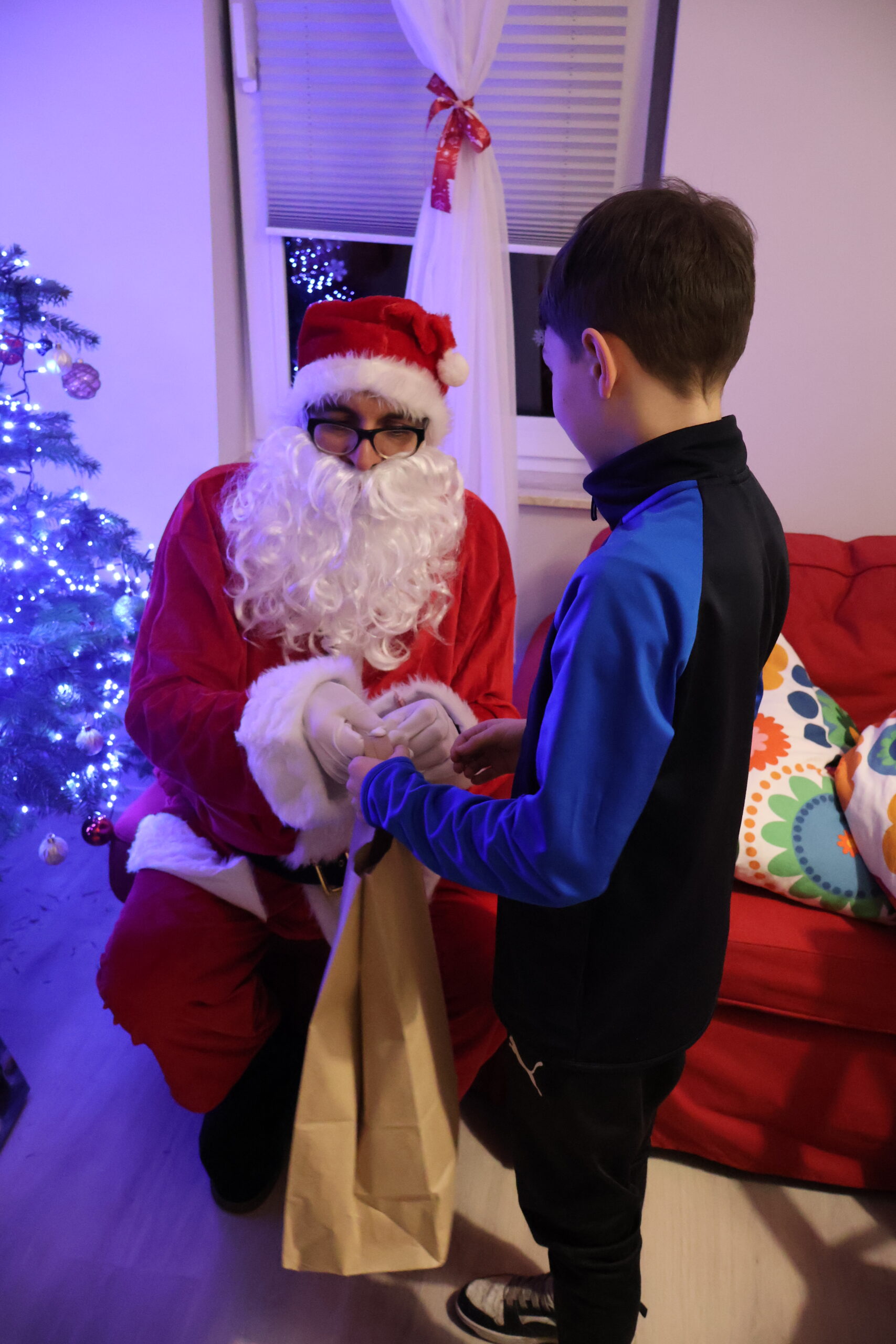 Mikołaj z AJP siedzi na pufie wręcza chłopcu ze świetlicy "Jaskółka" prezent