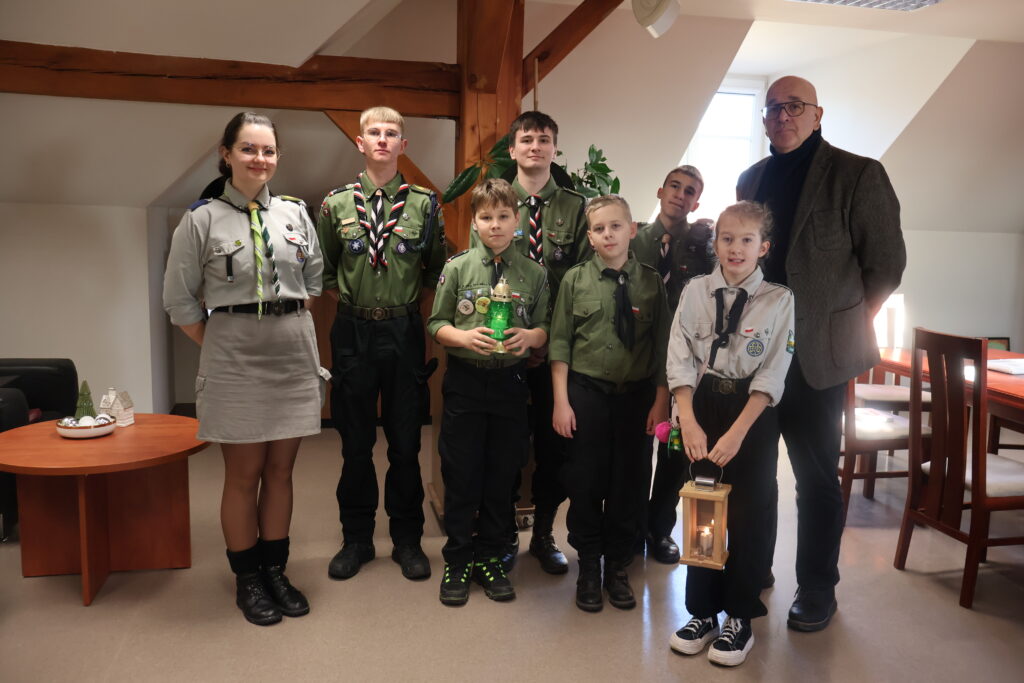 Grupa harcerzy z Gorzowa stoi w Rektoracie z Kanclerzem Uczelni. Dwójka dzieci na pierwszym planie trzymają lampion i znicz w ręku.