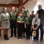 Grupa harcerzy z Gorzowa stoi w Rektoracie z Kanclerzem Uczelni. Dwójka dzieci na pierwszym planie trzymają lampion i znicz w ręku.