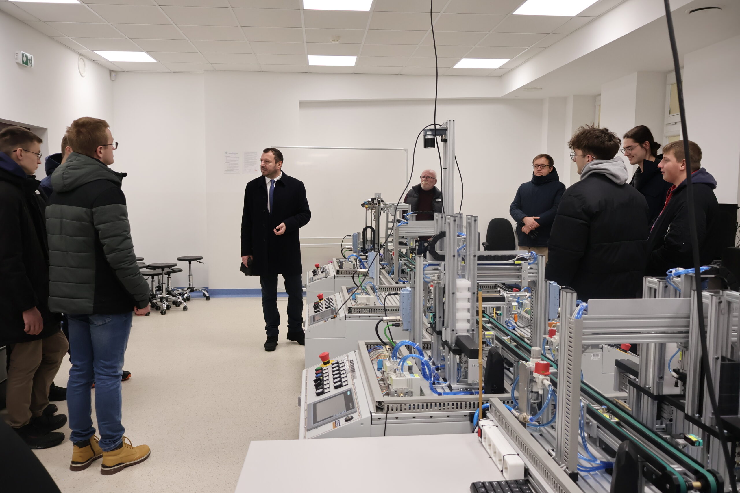 Grupa osób podczas zwiedzania laboratorium, obok nich stoją maszyny przemysłowe.