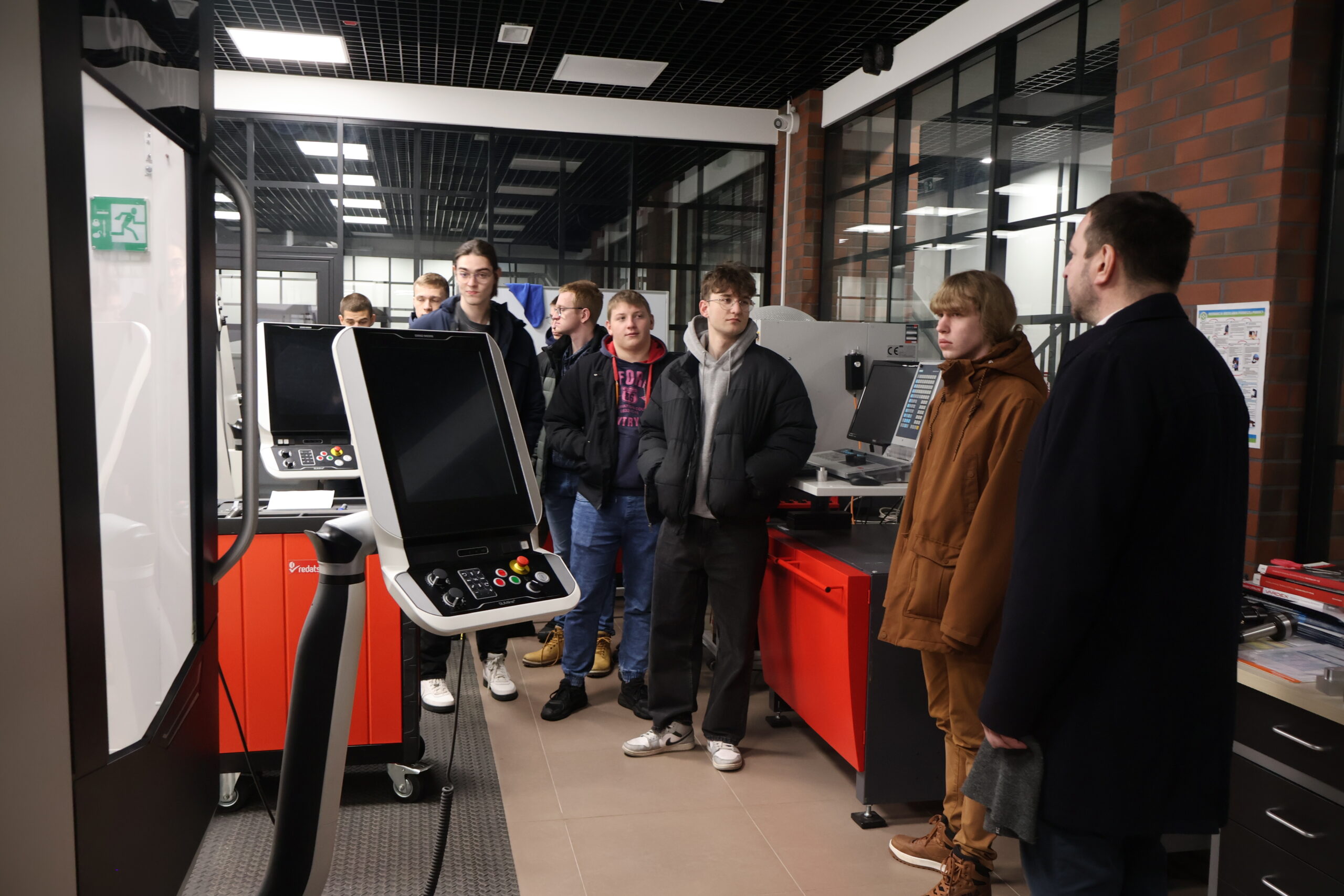 Grupa osób podczas zwiedzania laboratorium, obok nich stoją maszyny przemysłowe.