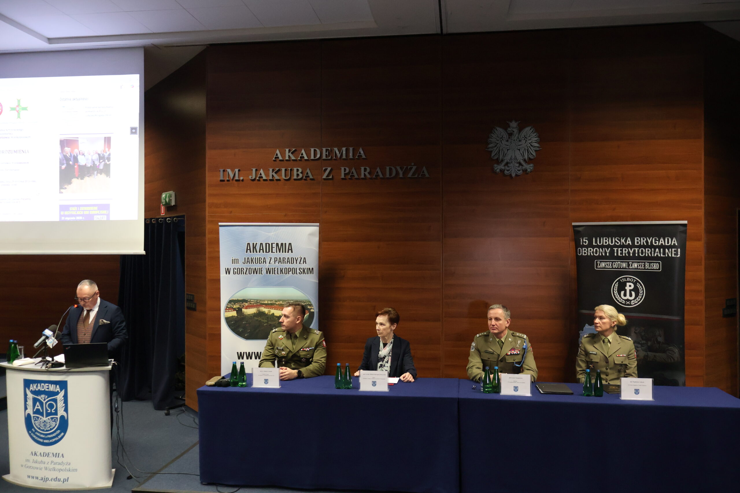 W auli im. prof. Stanisława Kirkora za mównicą wita wszystkich zgromadzonych i otwiera wydarzenie dr Wojciech Kuska. Za stołem prezydialnym siedzą od lewej: mjr rez. mgr dypl. Robert Urbanek, prof. dr hab. Elżbieta Skorupska-Raczyńska, płk Leszek Giergielewicz i major Magdalena Goliszek.