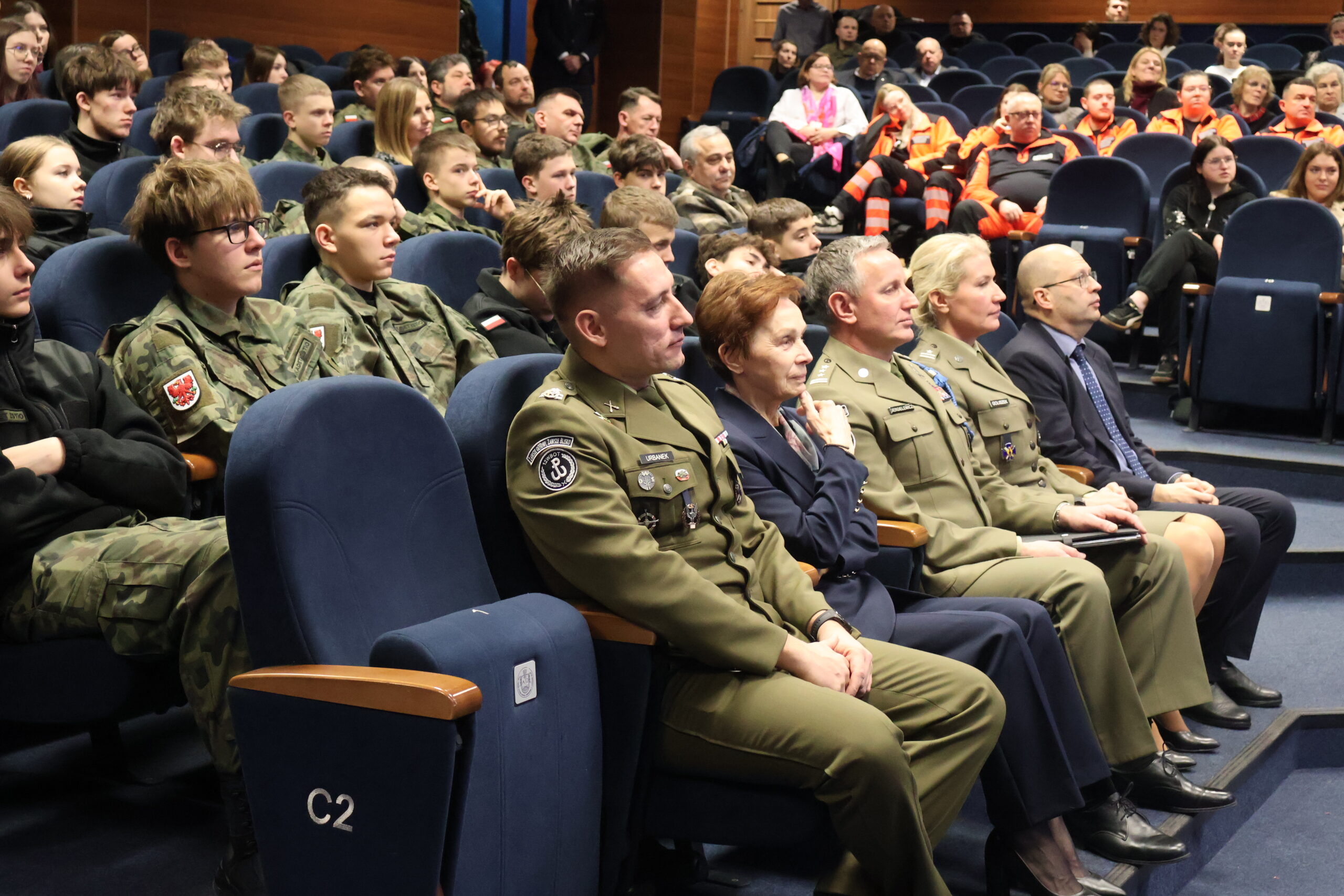 Na zdjęciu w auli im. prof. Stanisława Kirkora na zdjęciu widoczni w pierwszym rzędzie: mjr rez. mgr dypl. Robert URBANEK, prof. dr hab. Elżbieta Skorupska-Raczyńska, płk Leszek Giergielewicz, major Magdalena Goliszek i Radosław Wróblewski
