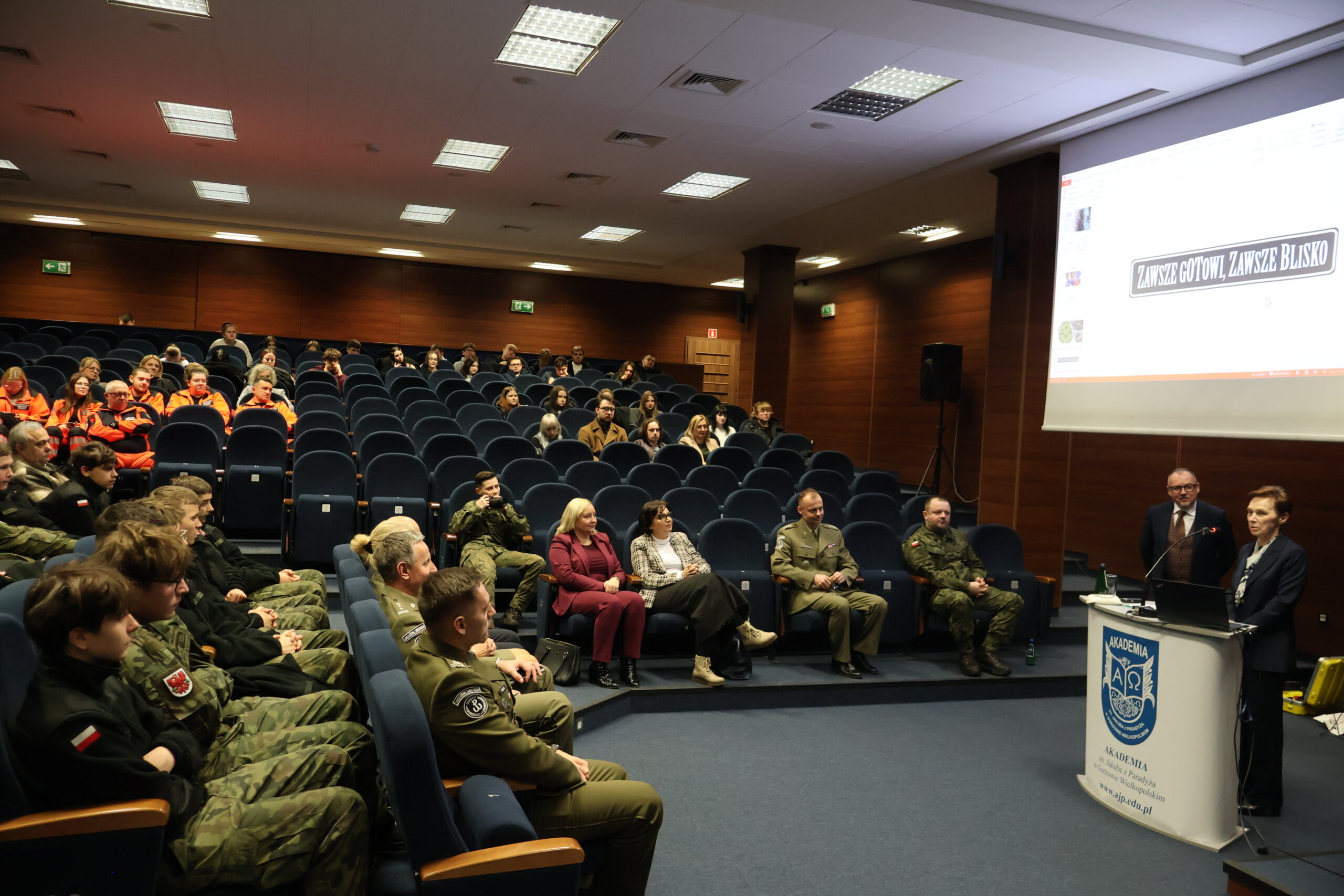 W auli im. prof. Stanisława Kirkora za mównicą stoi i przemawia na zakończenie prof. dr hab. Elżbieta Skorupska-Raczyńska Rektor Akademii im. Jakuba z Paradyża, a za nią slajd z napisem"ZAWSZE GOTOWI,ZAWSZE BLISKO". Rektor przemawia do zgromadzonych gości na auli, widoczni są Dziekani, Prorektor ds. Kształcenia, pracownicy Akademii oraz młodzież z gorzowskim szkół.