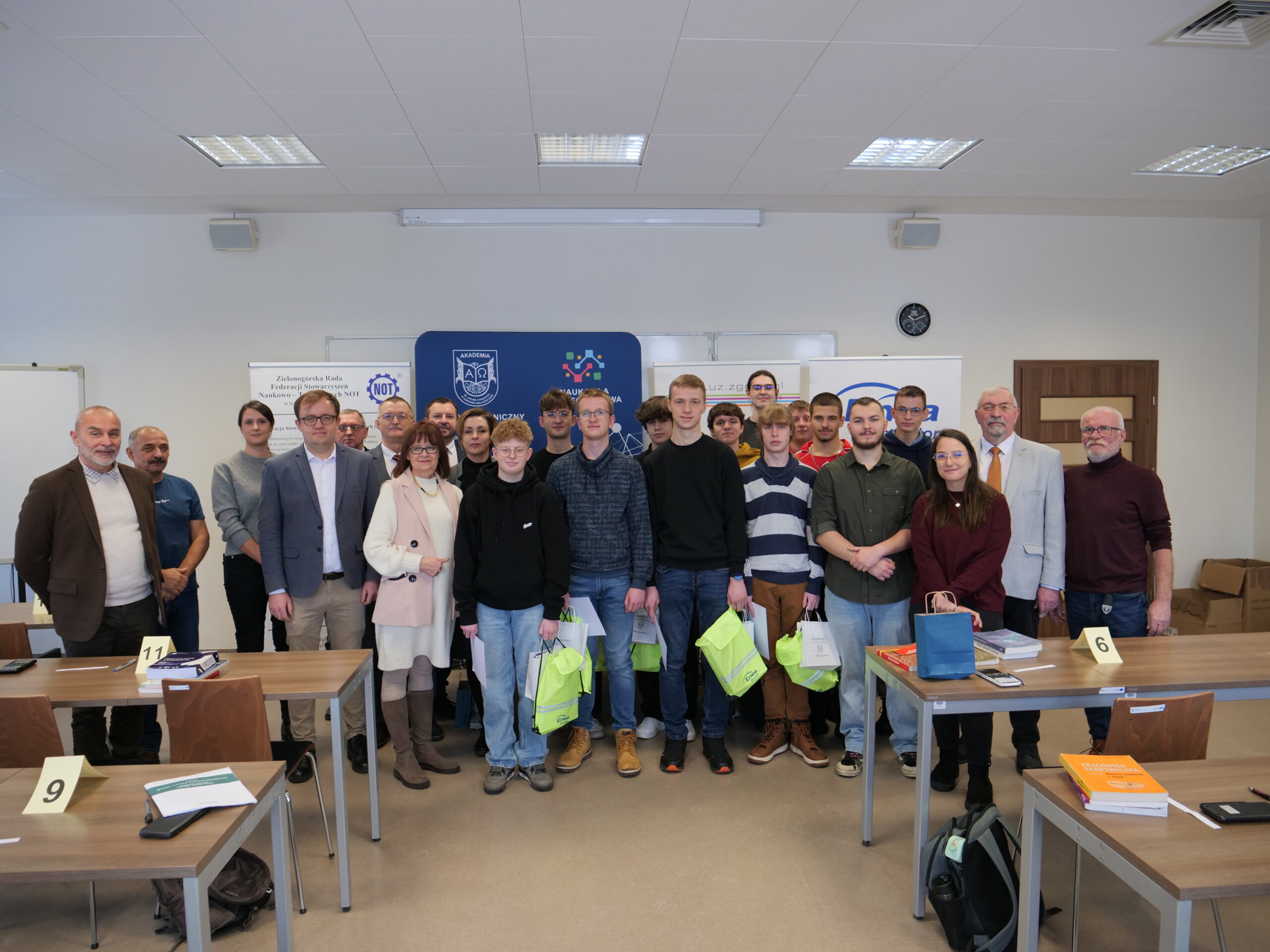 Uczestnicy oraz organizatorzy olimpiady stoją obok siebie. Uczestnicy trzymają w rękach nagrody.