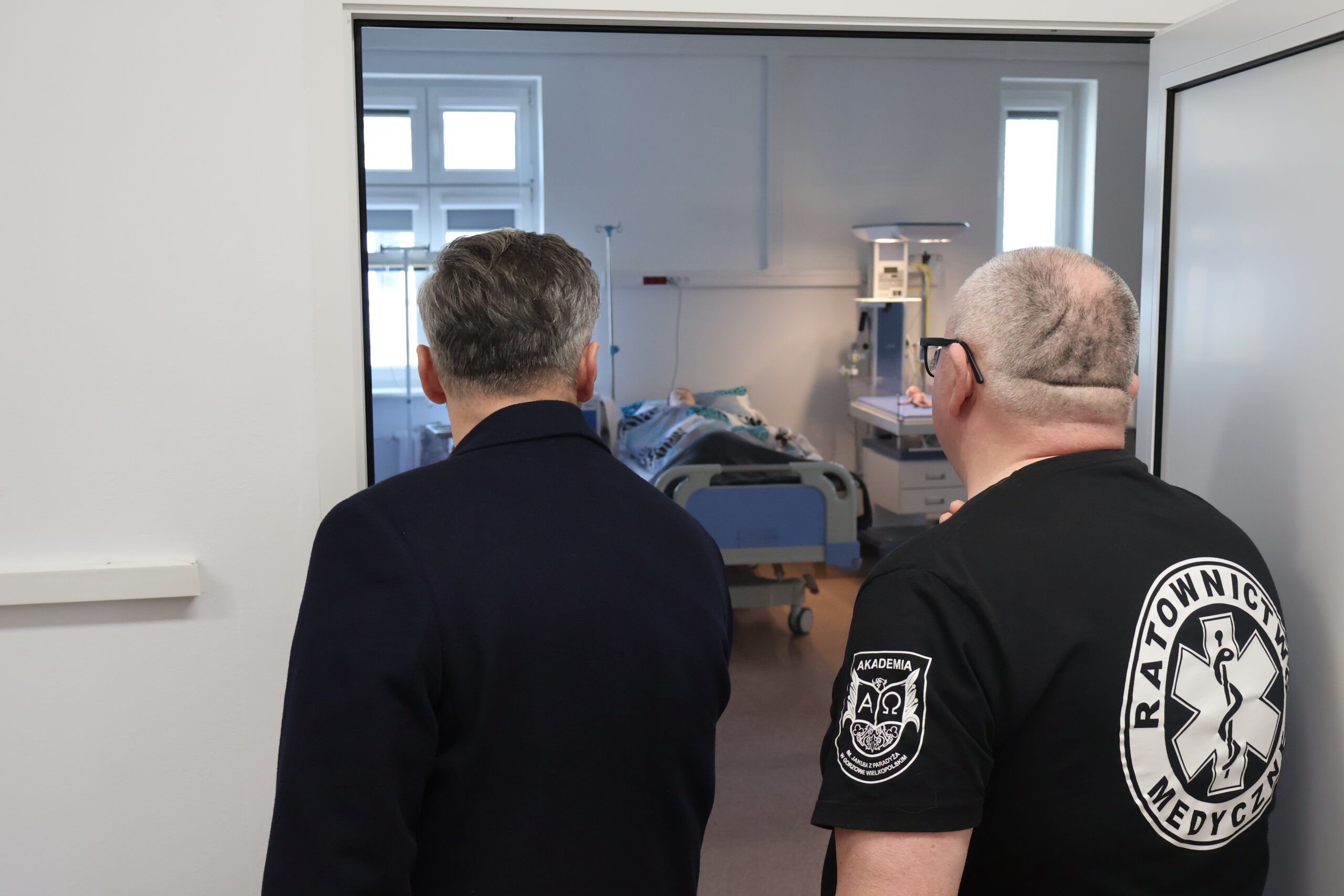 Na zdjęciu dwie osoby - po prawej pracownik Wydziału Nauk o Zdrowiu - Robert Sołtys ratownik medyczny oraz poseł Waldemar Sługocki wpatrujący się w gabinet pielęgniarstwa stoją od tyłu.