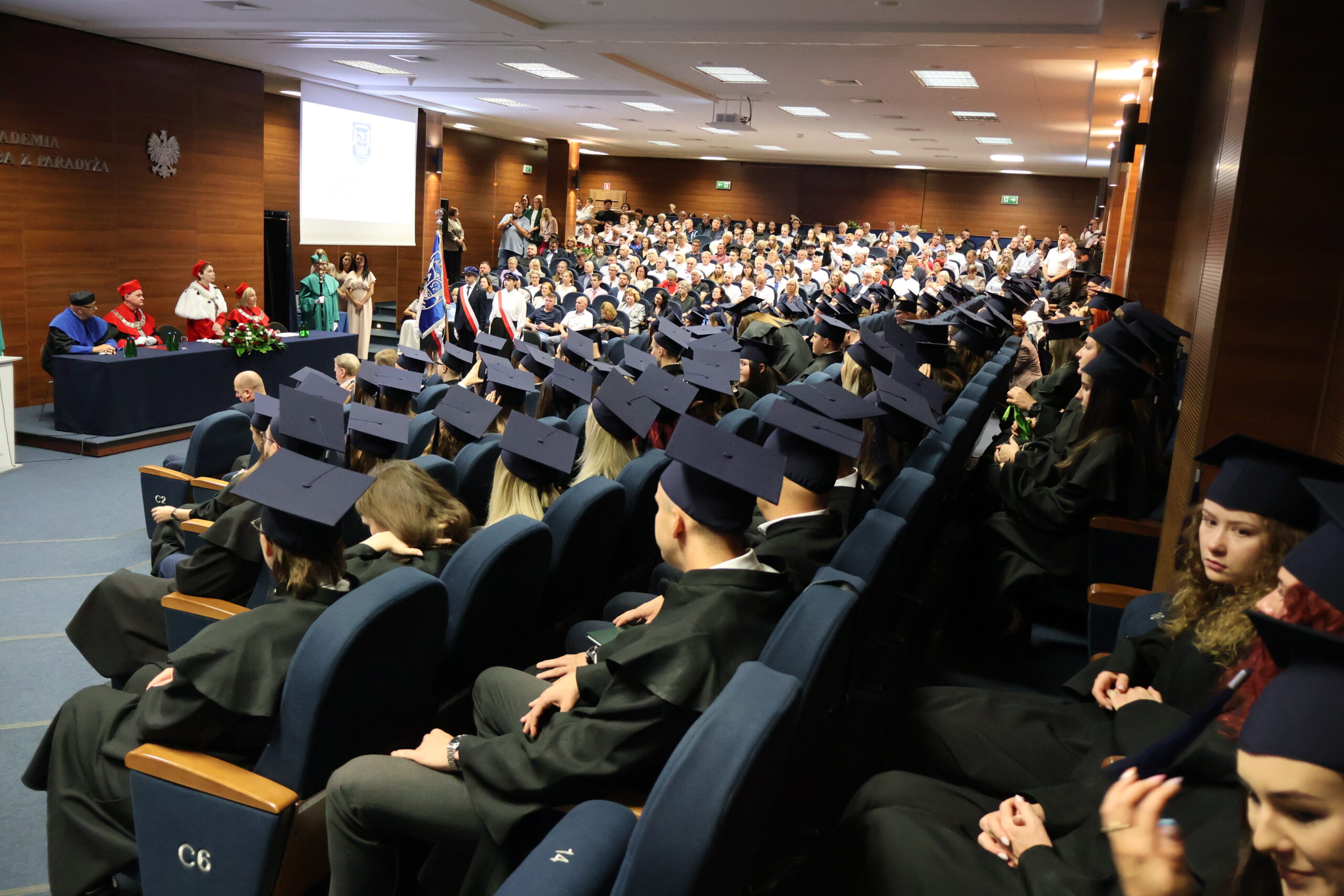Absolwenci siedzą w auli podczas absolutorium.