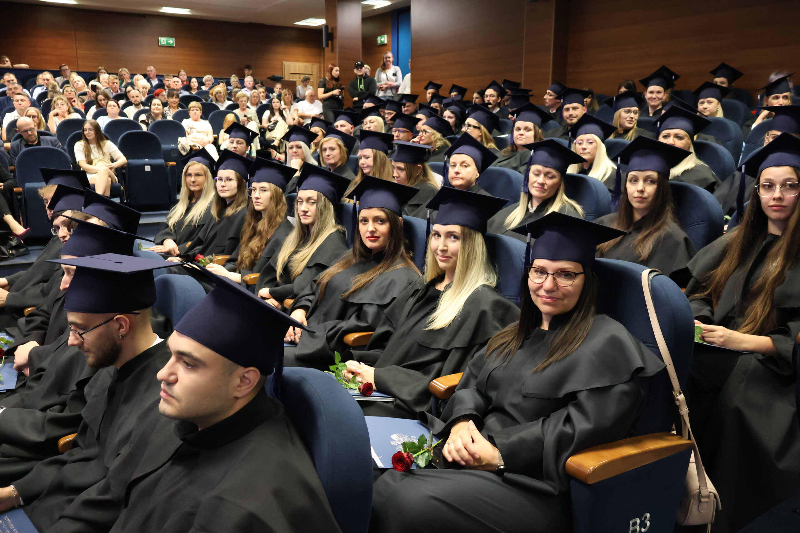 Grupa absolwentów siedzi w togach podczas absolutorium.