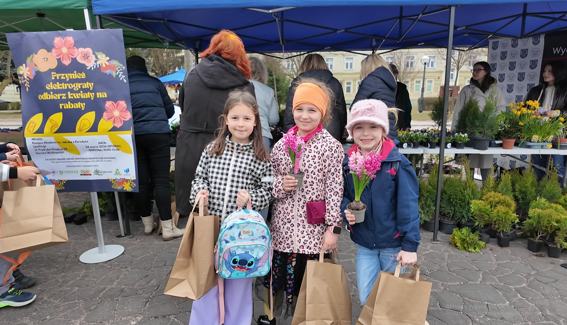 Trzy dziewczynki stoją trzymając kwiaty.
