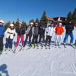 Dziesięciu uczestników zawodów stoi w rzędzie na stoku narciarskim.