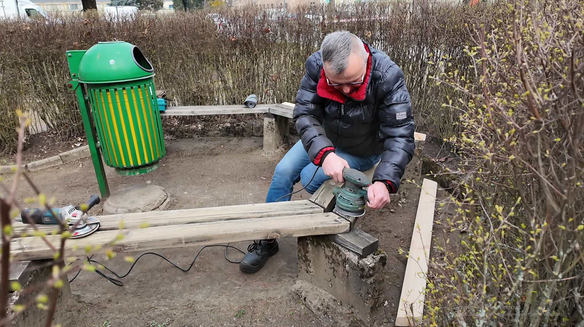 Mężczyzna oczyszcza (szlifuje) ławkę.