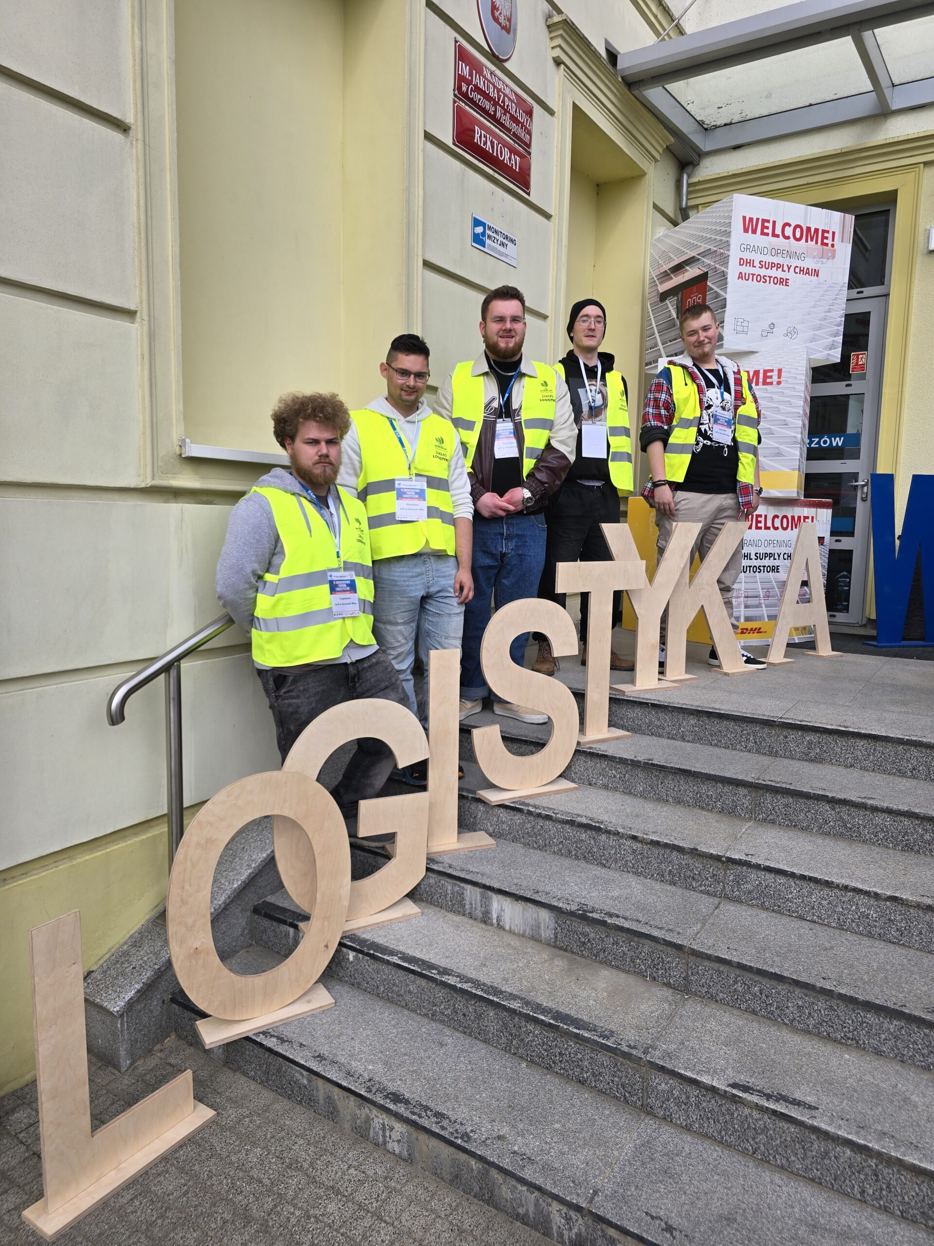 Pięciu studentów stoi przy napisie LOGISTYKA.