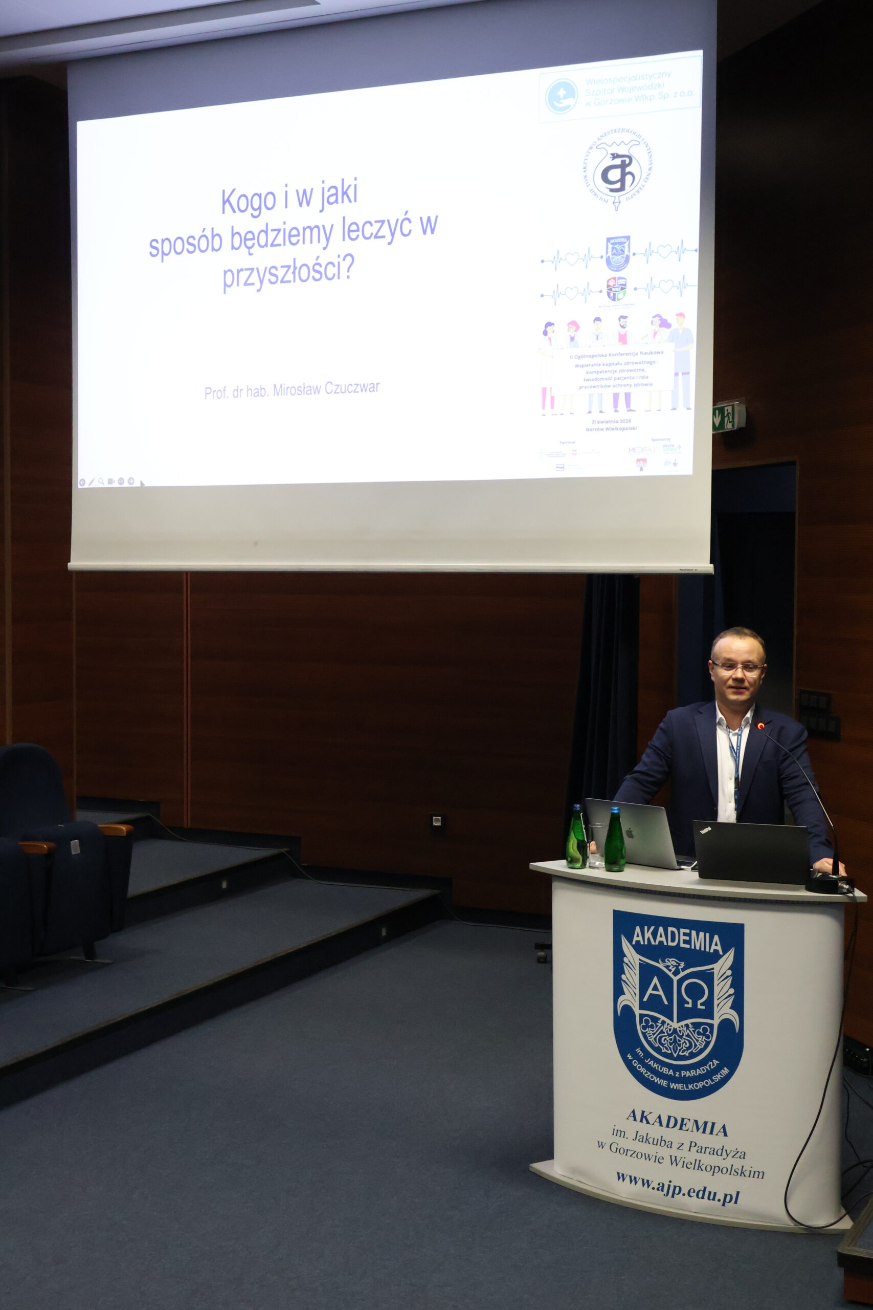 Prelegent stoi przy mównicy i prezentuje temat Kogo i w jaki sposób będziemy leczyć w przyszłości?