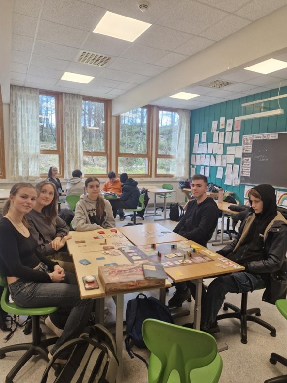 Obraz zawierający pomieszczenie szkolne, ławka i 5 osób gra w grę planszową