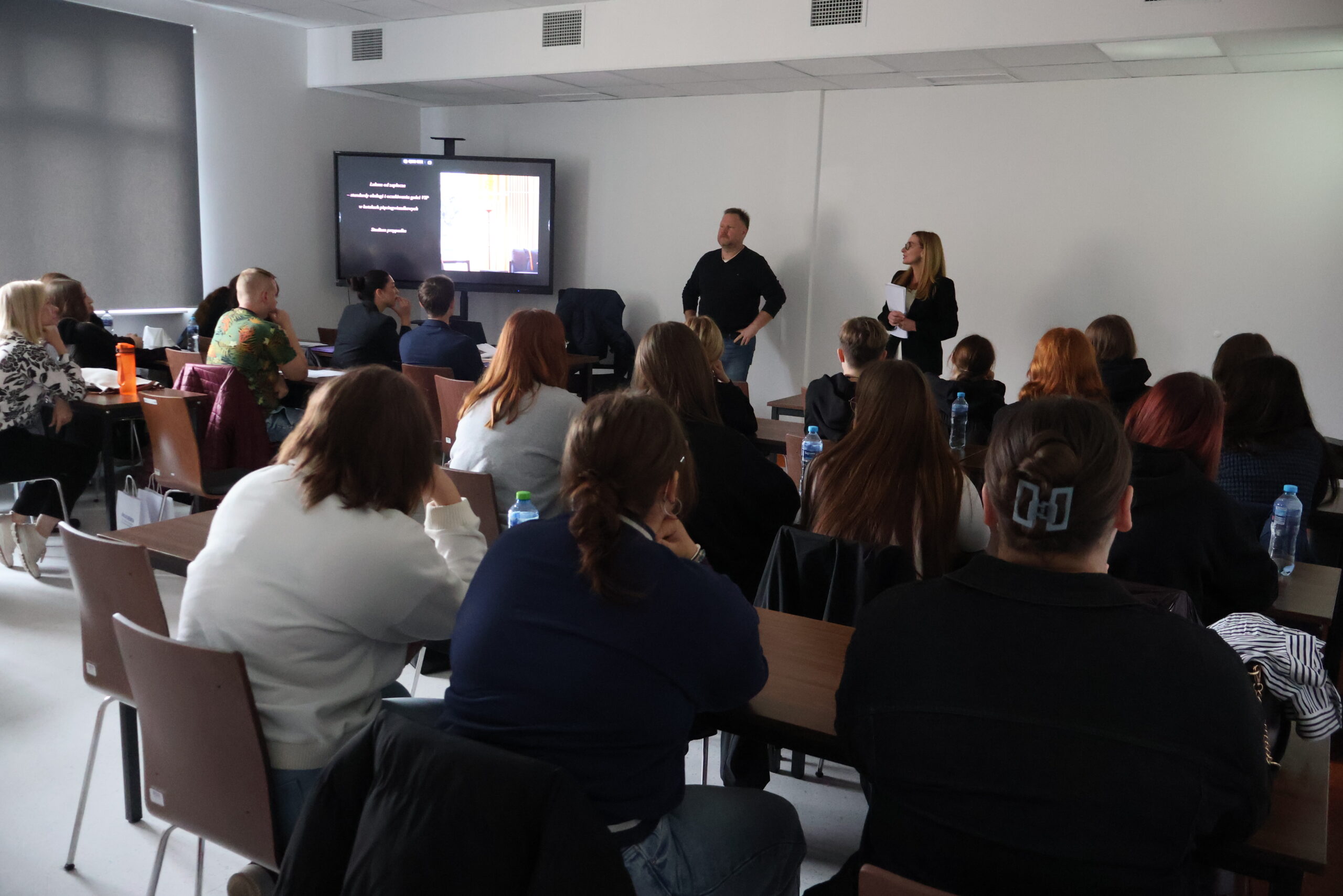 Uczestnicy Seminarium siedzą i słuchają wystąpienia prelegenta, obok stoi dr Sabina Ren