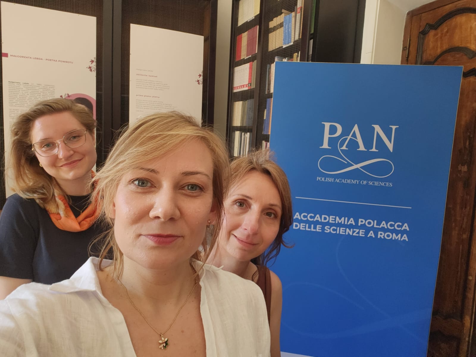 26. a. Trzy doktorantki na tle plakatu instytucji PAN-Stacji Naukowej w Rzymie
