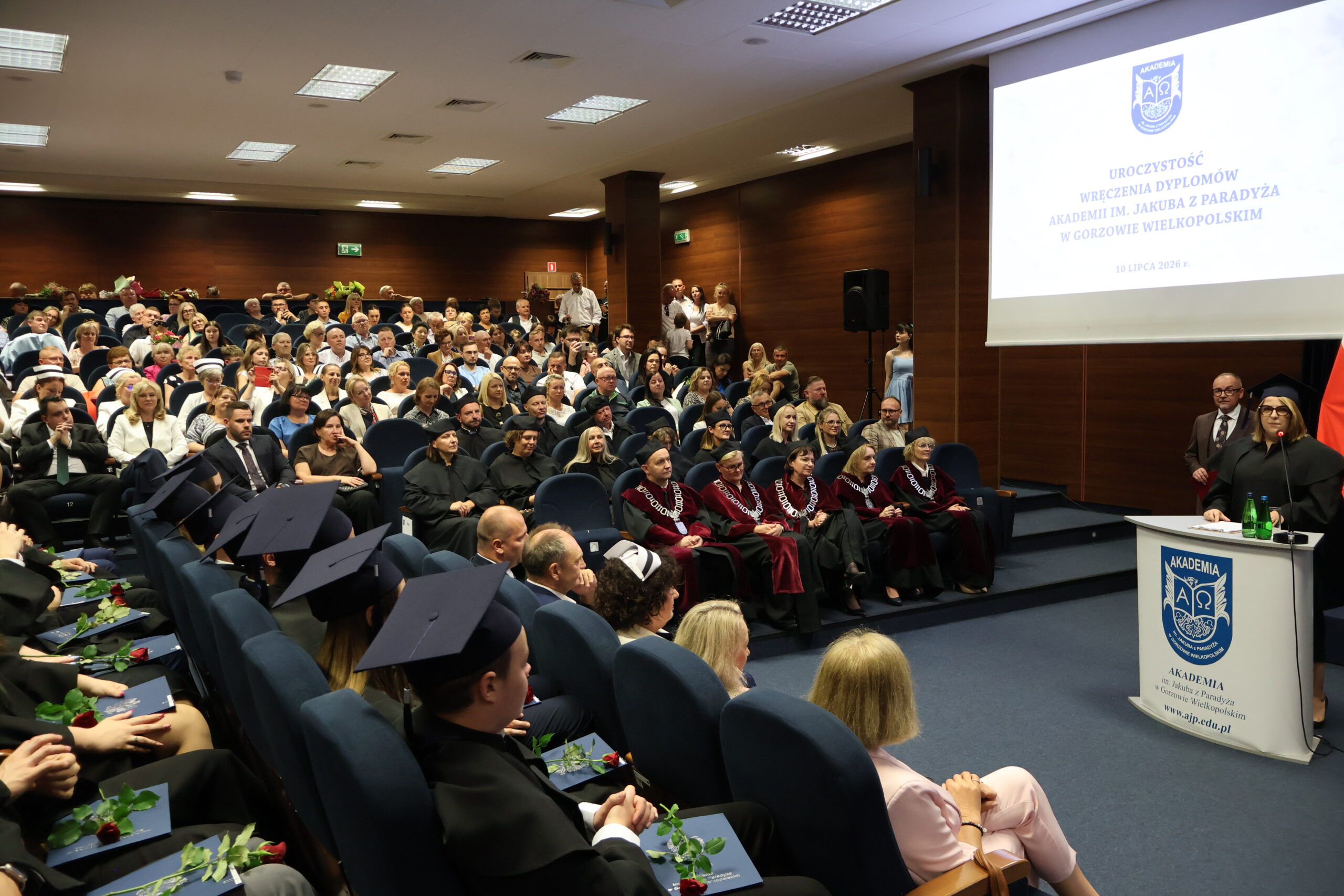 Uczestnicy Uroczystego Wręczenia Dyplomów oraz absolwenta przy mównicy podczas przemówienia.