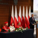 Władze Uczelni za stołem prezydialnym i Prezydent RP przemawia za mównicą.